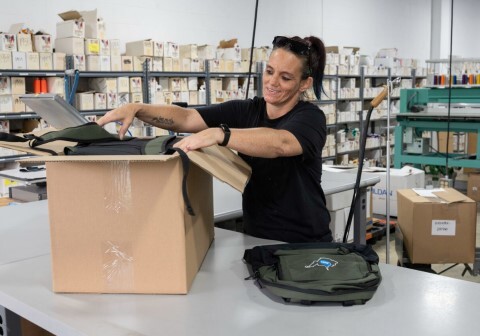 a woman placing embroidered items into a cardboard shipping box